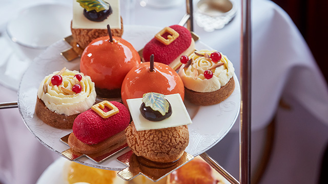 Christmas-themed cakes on two tiers of a cake stand, including cakes shaped like Santa's belt, cakes with holly leaves and cakes shaped like baubles.