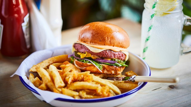 Plate of burger and fries with lemonade and ketchup in the background.