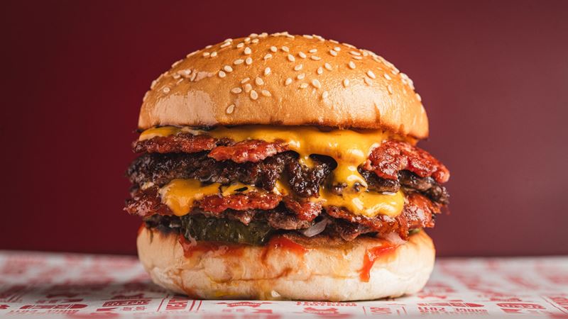 Prepare to get your hands dirty at MEATliquor with a stacked menu featuring top-tier burgers. Credit: Nic Crilly-Hargrave. Image courtesy of MEATliquor. A photo of a burger at MEATliquor from the side with two beef patties, bacon and American cheese on a sesame bun