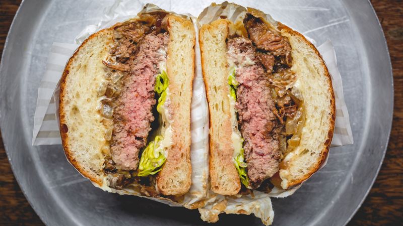 Share a photo of the FOMO-inducing burger cross sections at Patty & Bun. Credit: Justin DeSouza. Image courtesy of Patty & Bun. A bird's-eye photo of a Patty & Bun burger sliced in half, showing the thick beef patty pink in the middle with caramelised onions, lettuce and a mayo based sauce