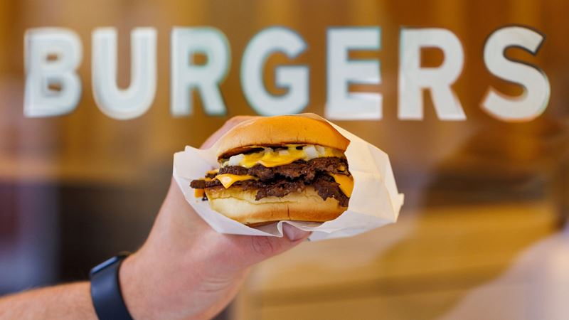 A photo of a hand holding the Supernova house cheeseburger in front of the "burgers" lettering on the shop window
