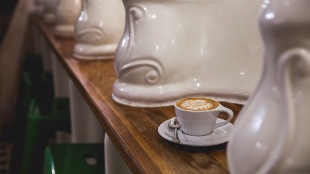 A cup of coffee on a wooden bar, set in between white porcelain urinals.