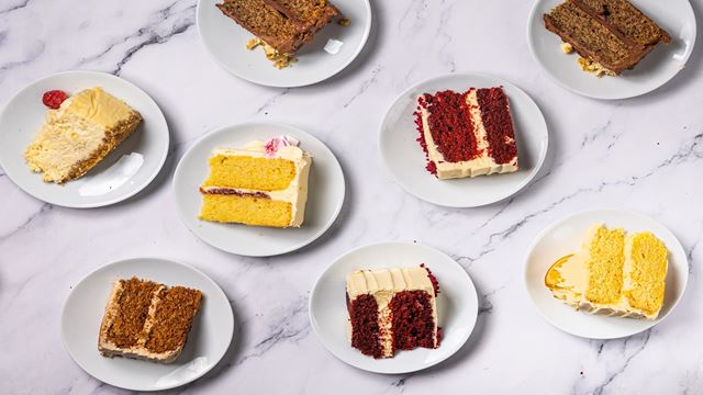 close up aerial photo of a marble table with 8 small white plates with cake slices on, including lemon cake, carrot cake and red velvet cake