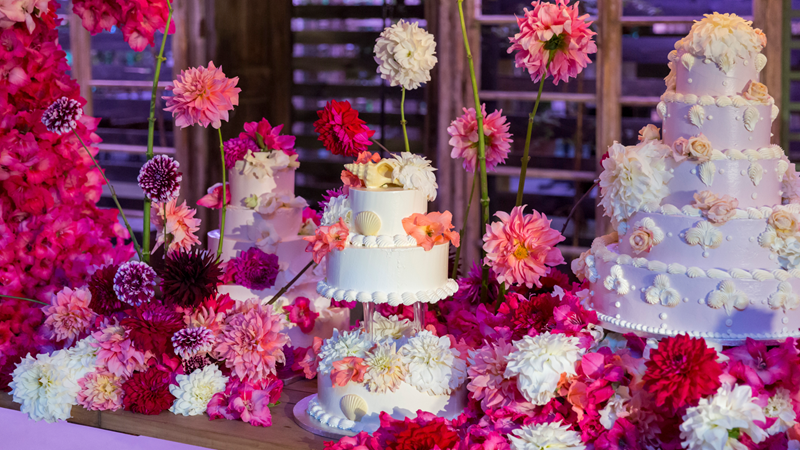 Customise your dream cake with Lily Vanilli in east London. Credit: Lily Vanilli. Image courtesy of Lily Vanilli. Three tiered celebration cakes each decorated with intricate pink, purple and white icing designs on a table surrounded by an arrangement of flowers in the same colours