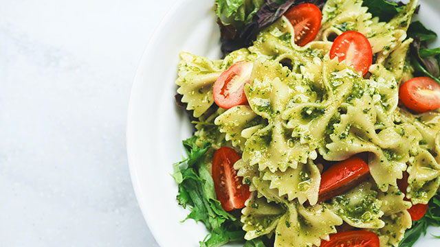 Dine on fresh pasta and tomatoes © Eaters Collective / Unsplash. Image courtesy of Eaters Collective / Unsplash. A plate of pasta bows with pesto, green leaves and red tomatoes