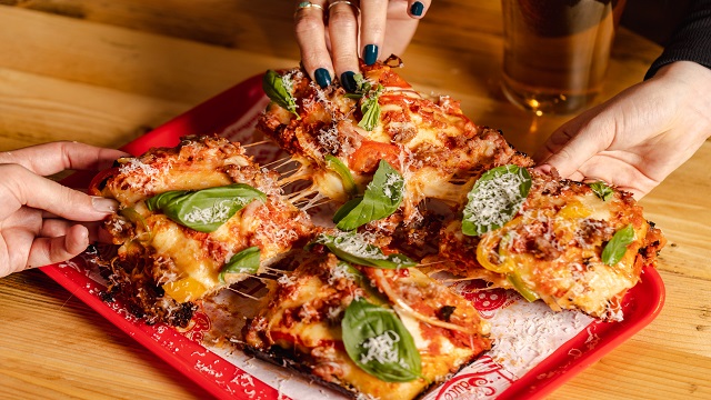Thick, square shaped pizza being pulled apart with stringy cheese showing
