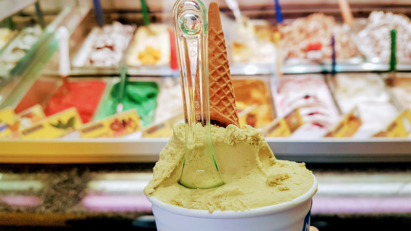 A person holding up a cup of ice cream with an upside down cone and spoon against the counter