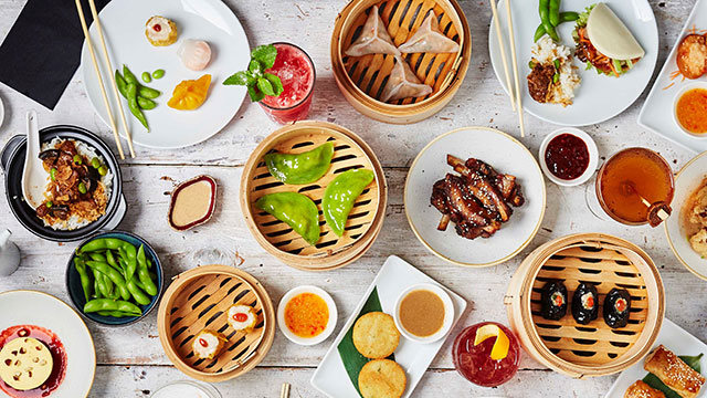 Feast on a selection of Asian flavours © Issy Oakes. Image courtesy of Issy Oakes / Ping Pong. An overhead shot of steamed Dim Sum, bao, buns and gyozas on a table with plates and chopsticks