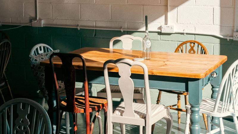 Catch up with mates at Against The Grain Cidery where cider takes centre stage. Credit: Jack Ducey. Image courtesy of Against The Grain Cidery. A photo of a wooden table at Against The Grain Cidery taproom with mismatching vintage chairs in different colours and a candlestick inside an empty wine bottle on the table with a ray of sun catching the walls