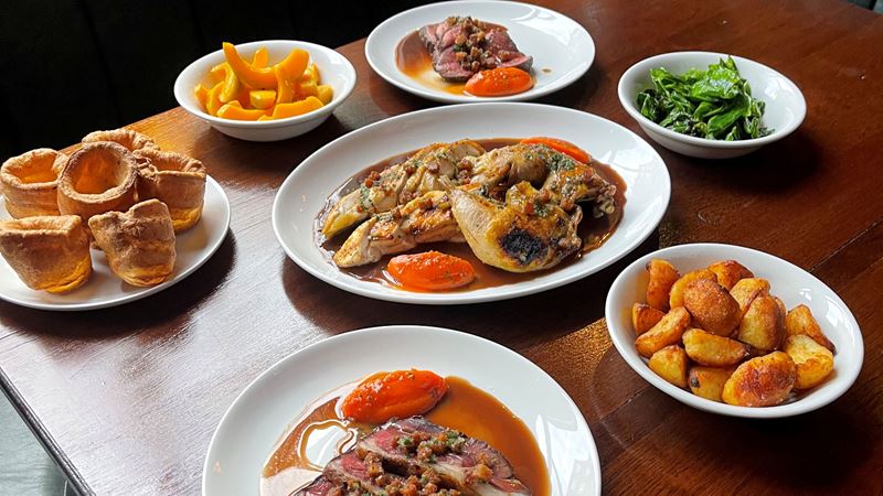 Delight in succulent roast meats and all the trimmings at The Parakeet in north London. Credit: The Parakeet. Image courtesy of The Parakeet. A photo of several dishes on a table at The Parakeet featuring a spread of roast chicken, pork, roast potatoes, butternut squash, cabbage and yorkshire puddings
