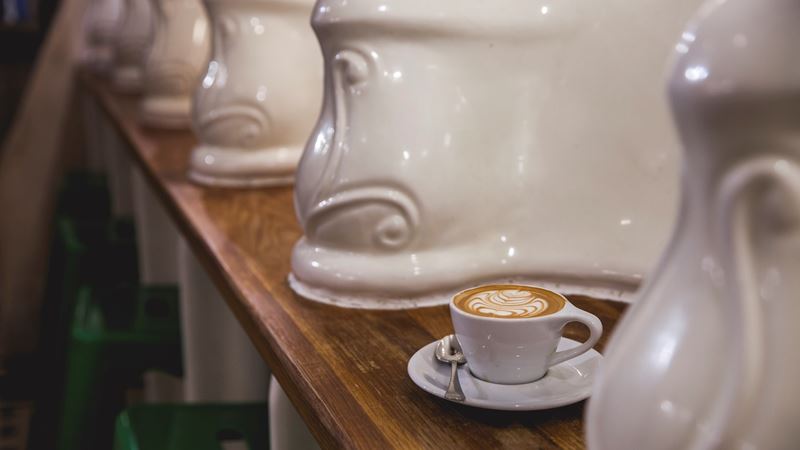 Experience Victorian bathrooms transformed into trendy coffee bars. Credit: The Attendant. Image courtesy of The Attendant. Cup of coffee on wooden counter surrounded by old Victorian urinals repurposed as decoration in quirky London cafe.