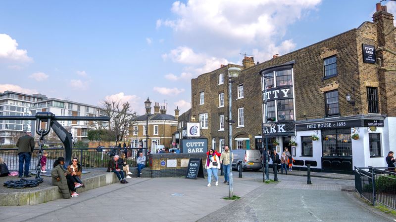 Head to the Cutty Sark tavern for scenic views of the Thames from Greenwich. Credit: Shutterstock. Image courtesy of Shutterstock. A photo of the exterior of the Cutty Sark pub in Greenwich with people walking on the street in front, a giant anchor sculpture and a snippet of the Thames on the left of the image