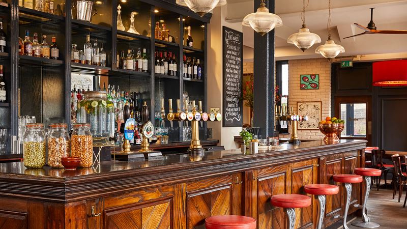 Inside a cosy pub in London, with a wooden bar area and drinks lined on shelves in the background.