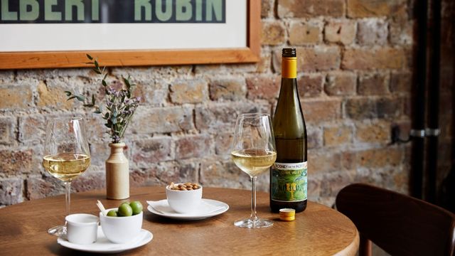 Pair fantastic wine with delicious bar snacks at Vinoteca. Image courtesy of Vinoteca. A brown table against a brick wall with bar snacks and glasses of white wine.
