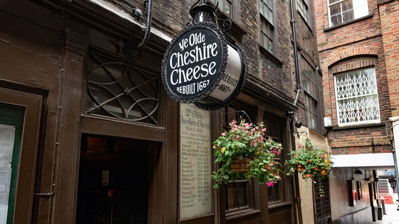Follow the hidden alley that leads to Ye Olde Cheshire Cheese, a legendary London institution. Credit: Shutterstock. Image courtesy of Shutterstock. A photo of the exterior of Ye Olde Cheshire Cheese with the round sign outside and hanging baskets with flowers in the windows