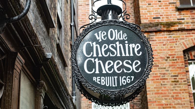 Ye Olde Cheshire Cheese is one of London's cosiest pubs. Credit: Shutterstock. Image courtesy of Shutterstock. Ye Olde Cheshire Cheese pub sign with pub name in white letters on a black background, with the inscription 'rebuilt in 1667' and brick walls in the background.