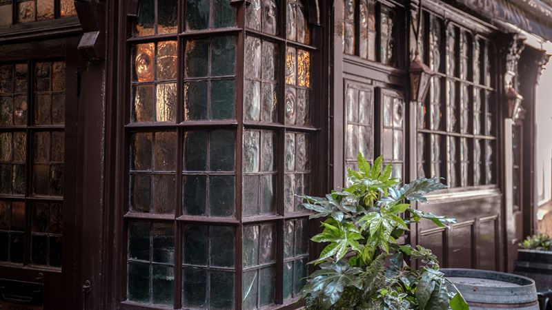 Sip on your drink of choice at Ye Olde Mitre - a pub with links to royalty and the world of film. Credit: Shutterstock. Image courtesy of Shutterstock. A photo of the exterior of Ye Olde Mitre with its old glass windows and dark red painted wood with a plant outside and warm lighting shining through