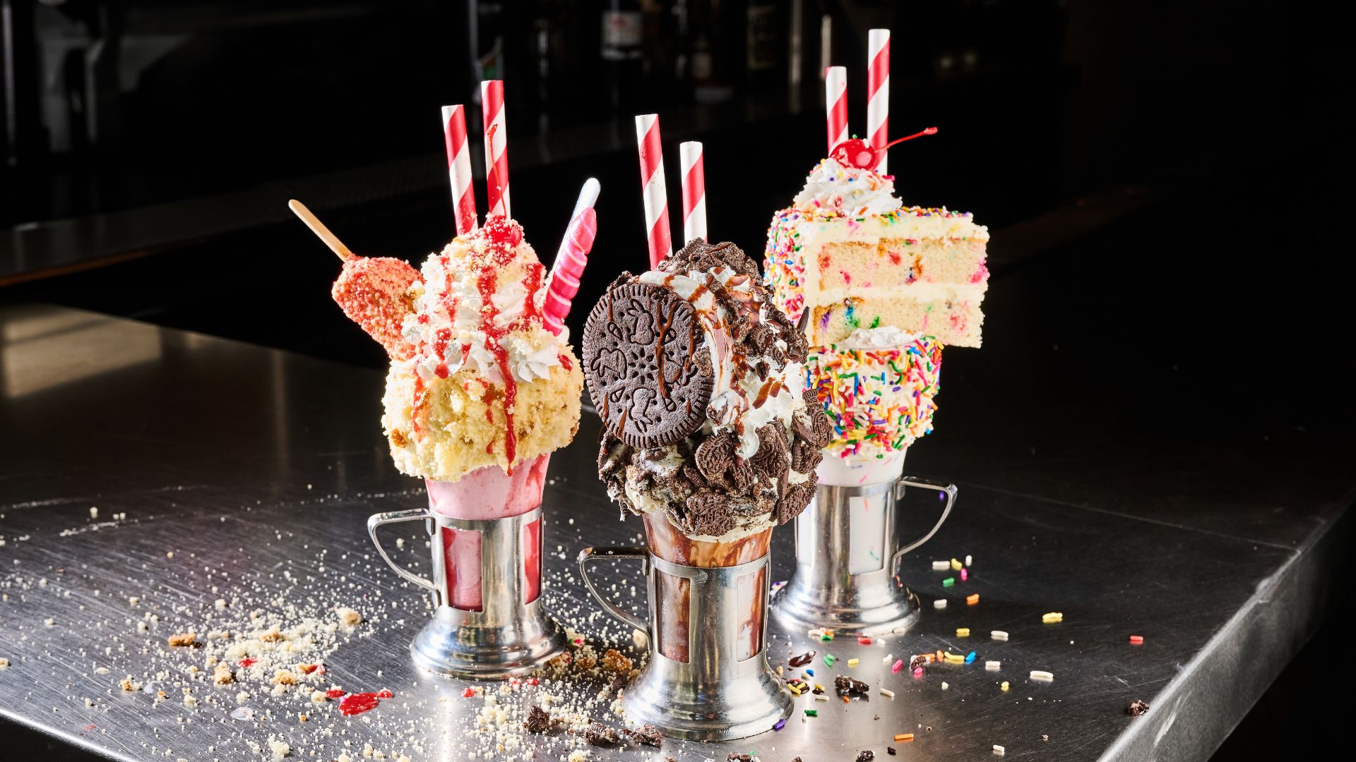 Enjoy award-winning eats, over-the-top CrazyShake® milkshakes and killer craft beers at Black Tap, Soho. Image courtesy of Bacchus Agency. Three cups of filled crazy shakes with cookies and cake and sprinkles at black tap london.