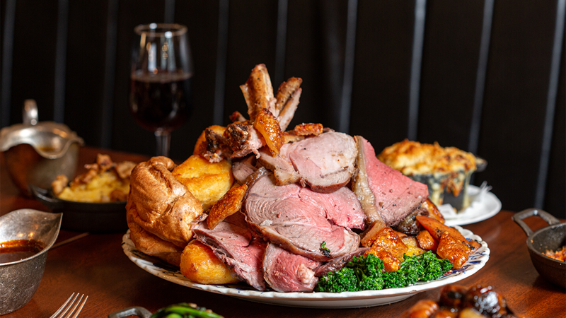 Feast on a traditional Sunday roast at Blacklock Soho. Credit: Rebecca Hope. Image courtesy of Blacklock. A plate piled high with roast meat, potatoes and vegetables, set on a wooden table with side dishes surrounding the plate