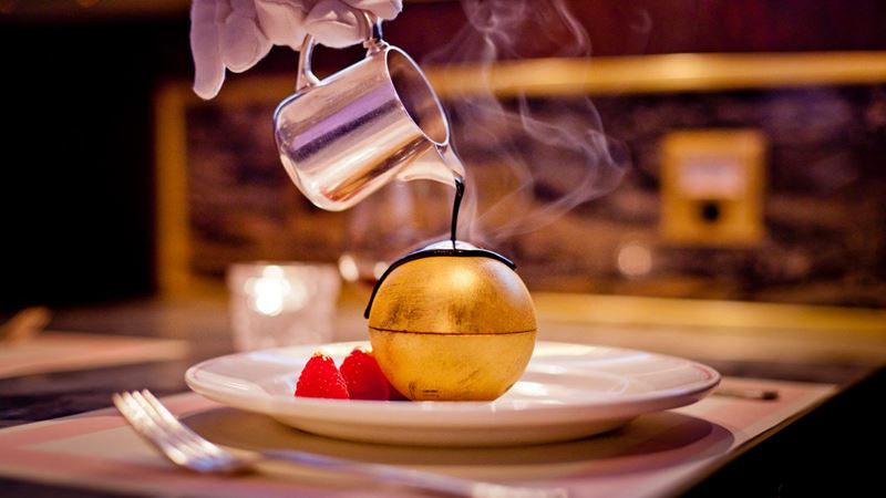 Treat your loved one to a delicious chocolate and raspberry dessert. Credit: Bob Bob Ricard. Image courtesy of Bob Bob Ricard. Close-up of hot chocolate being poured over a dessert hidden inside a golden chocolate dome, with raspberries on the side on a white plate at Bob Bob Ricard in London.