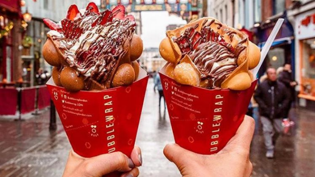 Two hands holding bubblewraps in a cardboard sleeve, stuffed with ice cream, strawberries and chocolate sauce