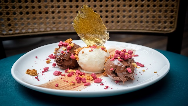 Large white flat bowl with three scoops of ice cream in the middle, covered in crushed honeycomb and a shard of caramel