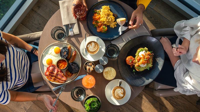 An aerial image of three people having brunch, including a full English, avocado on toast, scrambled eggs and coffee.