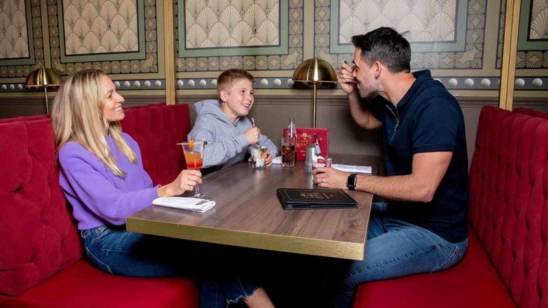 A family sit together in a red booth at the Monopoly-themed Top Hat Restaurant as the father and son share a sundae and the mother sips on an orange drink