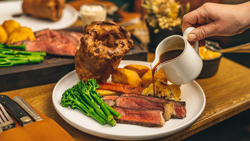 Roast dinner at The Harwood Arms. Credit: Lateef Okunnu. Image courtesy of The Harwood Arms. A table spread of roast dinners, with gravy being poured onto the plan in a small white jug
