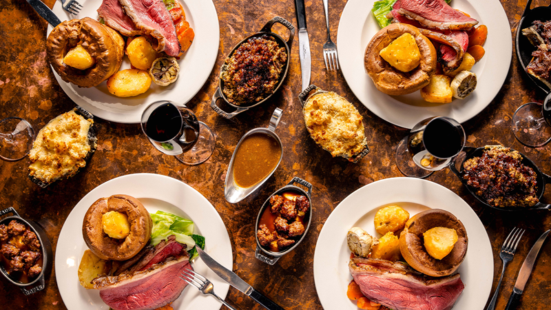 Four plates of Hawksmoor's Sunday roast with roast beef, vegetables, gravy and glasses of wine