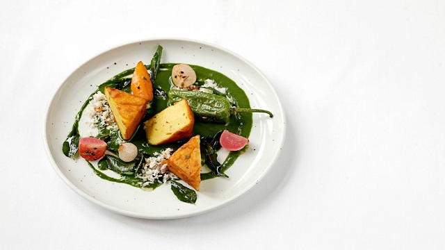 Chickpea gnocci served at The Cinnamon Club. Image courtesy of The Cinnamon Club. high angle shot of a small white plate with green sauce drizzled and chickpea gnocchi