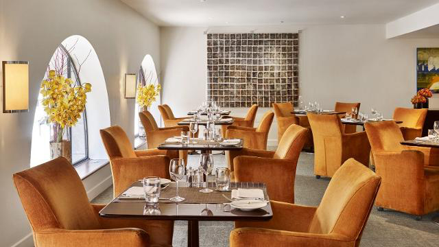 Rusted orange chairs at brown tables with yellow flowers in the windows of indigo restaurant in london.