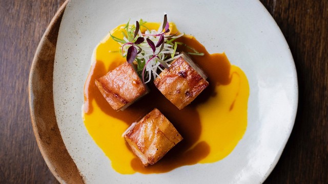Three pieces of braised Iberico pork on a white plate, served with a yellow sauce and salad, at Lima London.