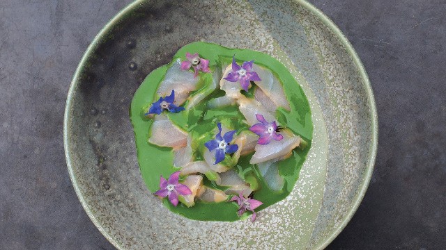 Indulge in some of the best ceviche in London at Peruvian restaurant Floral by Lima. Image courtesy of Lima London. Sea bass ceviche with green sauce and edible purple flowers presented in a grey dish at Peruvian restaurant Floral by Lima in London.
