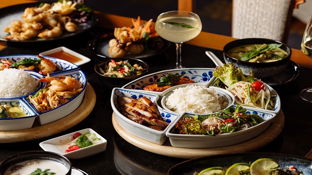 high angle shot of a table full of Thai food in sharing bowls, with cocktails placed on the table in between the dishes