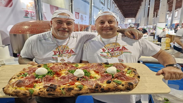 Metre long pizzas at Pizza Metro Pizza. Image courtesy of Pizza Metro Pizza. Two men in waiter uniform, holding a board with a metre long pizza on