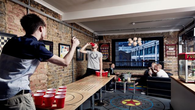 Polo Bar in London. Image courtesy of Polo Bar. a brick-wall exposed bar lounge, with two people playing beer pong and a group of people enjoying drinks in the background