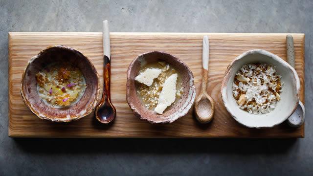 Three Bears Porridge at Restaurant Story. Image courtesy of Restaurant Story Three bowls filled with different types of porridge and large spoons on a long wooden board.