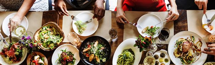 birds-eye view of people sat at a long dining table eating, with various small sharing plates in the middle