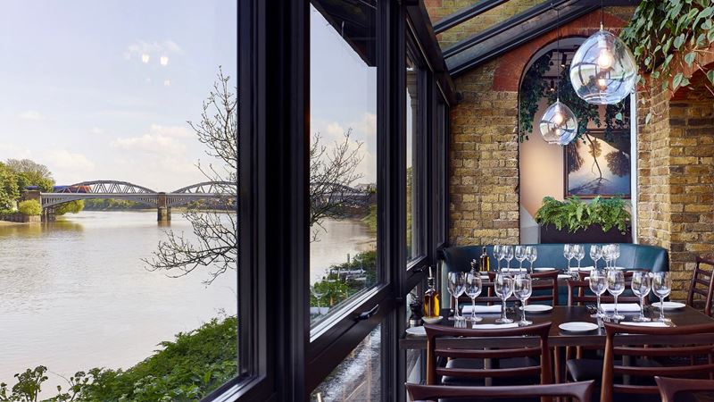 Rick Stein's restaurant in Barnes with wooden tables and chairs, brick walls and big open windows overlooking the river Thames.