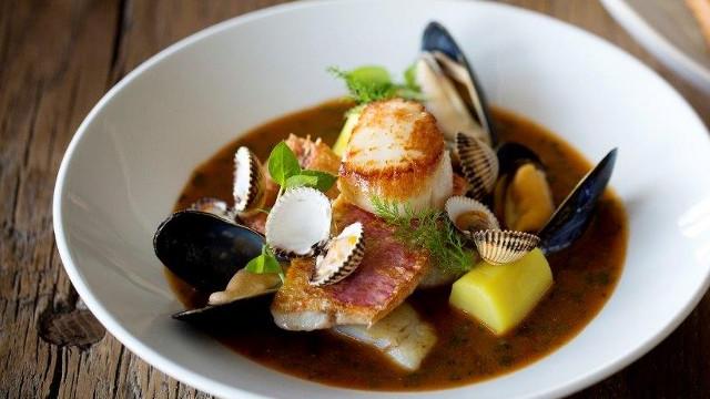 A white bowl filled with seafood stew with fresh scallop, muscles and vegetables.