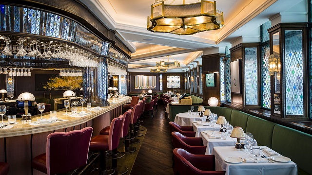 The Ivy bar and tables featuring red chairs, green banquette seating, while table cloth and dark wooden floors.