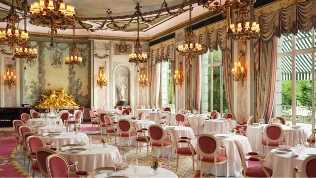 Discover delicious food in a beautiful setting at The Ritz Restaurant in London. ©Jack Hardy. Image courtesy of The Ritz London. A cream chandelier lit dining room with white tables and red chairs at the ritz restaurant in london.