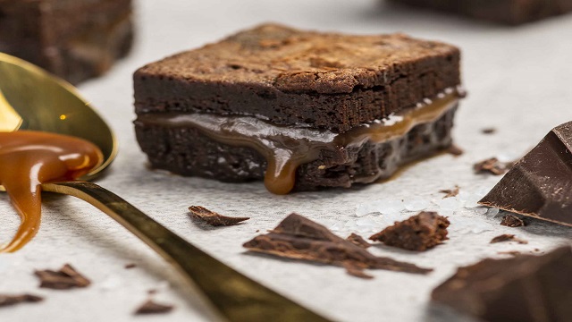 Landscape image of a thick chocolate brownie with a layer of salted caramel in the middle, drizzling down