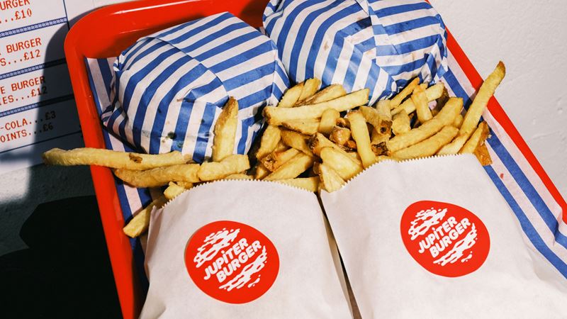 You can't go wrong with a juicy smash burger from Netil Market's Jupiter Burger. Credit: Teo Della Torre. Image courtesy of Jupiter Burger. A photo of two burgers wrapped in striped paper and hand cut fries in white bags with the Jupiter Burger logo on a red tray