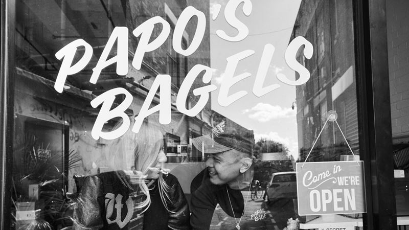 Bite into freshly baked New York-style bagels from the team at Papo's Bagels in Dalston. Credit: Kyle DeVre. Image courtesy of Papo's Bagels. A photo of the exterior of the Papo's Bagels store with the owners in the window and a come in we're open sign