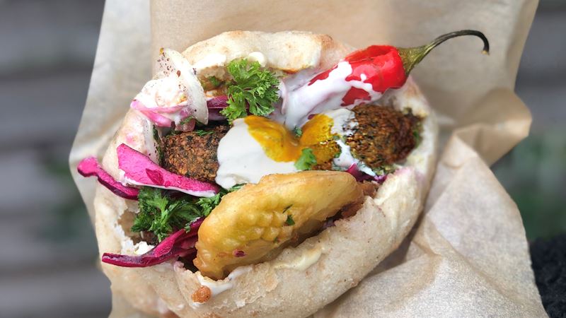 A photo of the falafel pitta from Pockets stuffed with fresh falafels, a deep fried potato, pickled red onions, a red chilli, lashings of sauce and topped with parsely
