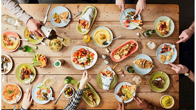 A large table with many plates of food with people eating and drinking