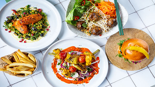 A selection of different vegan dishes such as plant based burger, kebab and stir fry,  presented on individual plates.