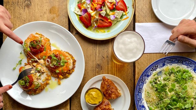 A selection of vegan dishes and a pint of beer laid out on a wooden table, viewed from above.